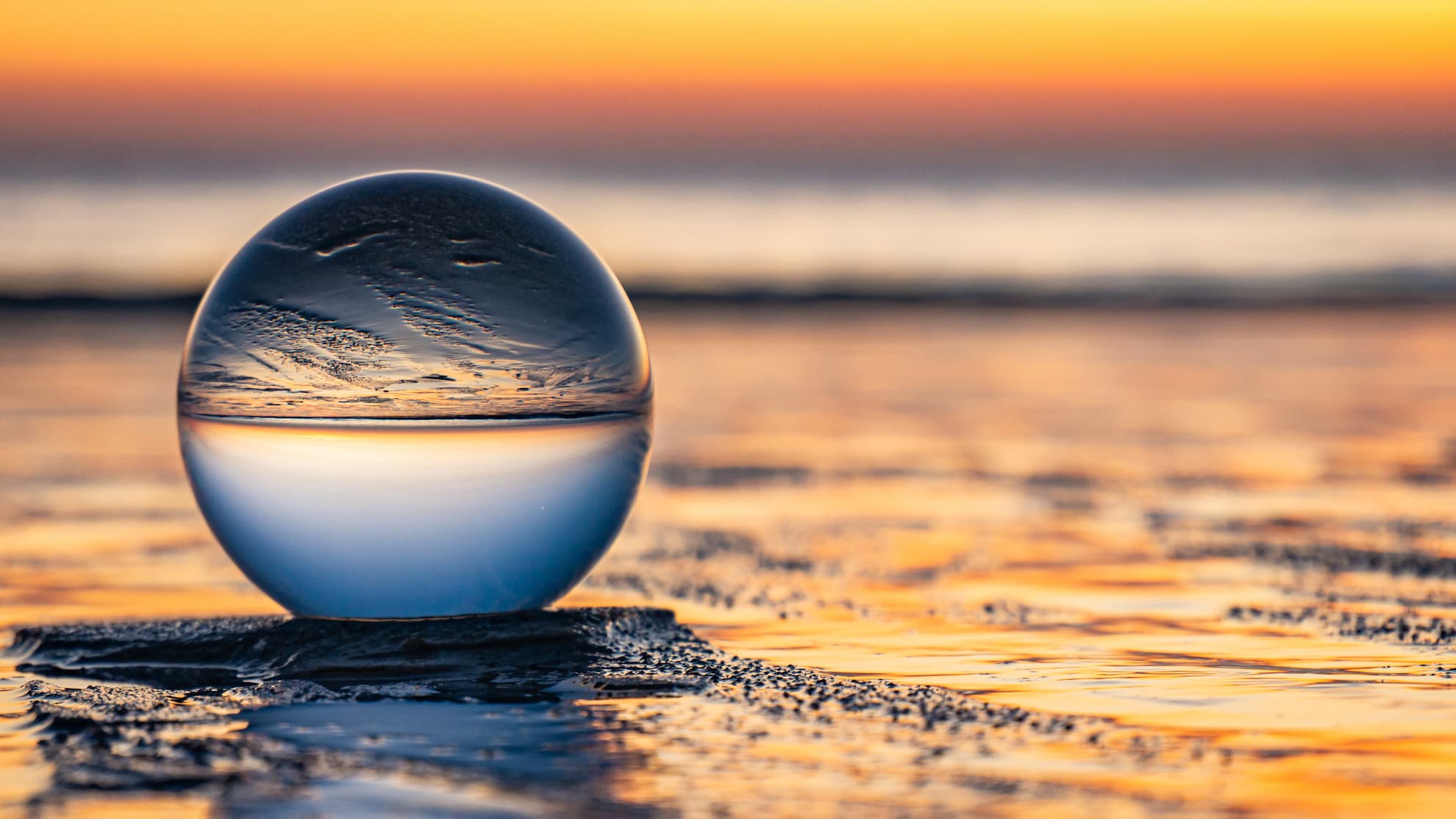 Eine Glaskugel am Wasser, in der sich ein Sonnenuntergang spiegelt.